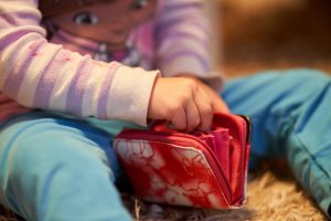 3 year old caucasian girl child is playing with money and red wallet